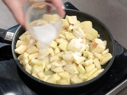 Ajout du sucre en poudre sur les morceaux de pommes dans la poêle