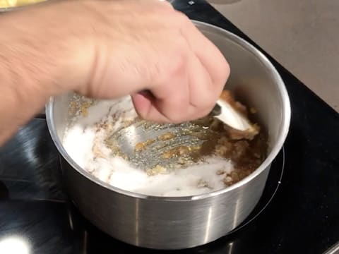 Le sucre qui est en train de cuire dans la casserole est mélangé à l'aide d'une spatule maryse