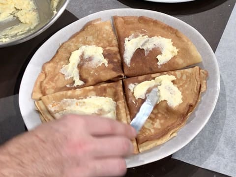 Du beurre d'orange ramolli est tartiné sur les crêpes à l'aide d'une petite spatule métallique coudée