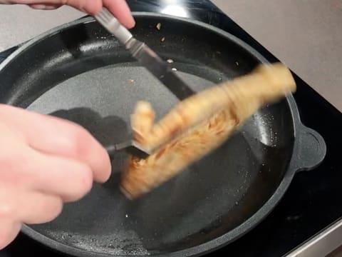 La crêpe est retournée dans la poêle, à l'aide de deux petites spatules métalliques coudées