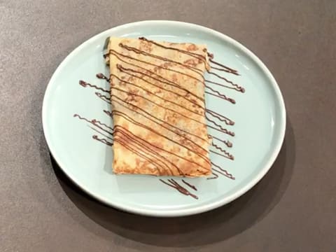 Obtention de la crêpe décorée avec des filaments de pâte à tartiner, sur l'assiette de service