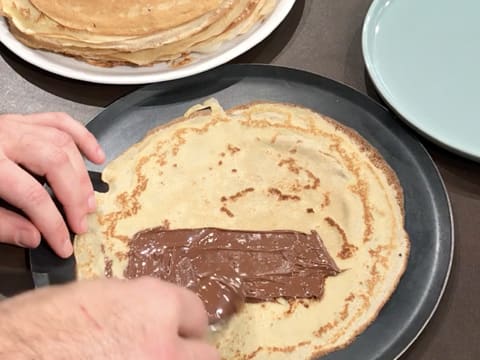 De la pâte à tartiner est étalée avec une petite cuillère, sur une moitié de la crêpe