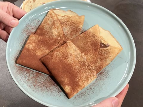 Obtention de deux crêpes au chocolat dans l'assiette de service, saupoudrées de cacao en poudre