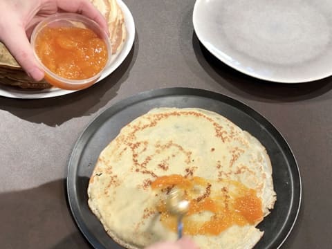 La confiture d'abricot est étalée sur la moitié de la crêpe avec la cuillère à café