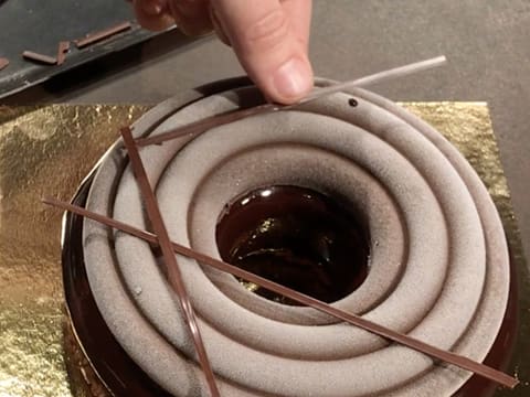 Un bâtonnet en chocolat est déposé sur des points de glaçage chocolat pochés sur l'entremets au chocolat de Pâques