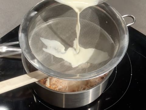La crème est versée dans une passoire fine au-dessus du caramel qui se trouve dans la casserole