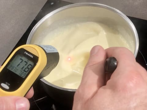 Prise de la température de la crème qui est en train de cuire dans la casserole, à l'aide d'un thermomètre électronique qui affiche 77,8°C