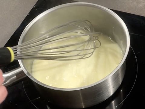 La crème est mélangée au fouet dans la casserole qui se trouve sur la plaque de cuisson