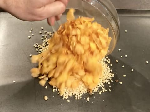 Les corn flakes sont versés sur la plaque à pâtisserie qui contient les noisettes hachées et les pignons de pin