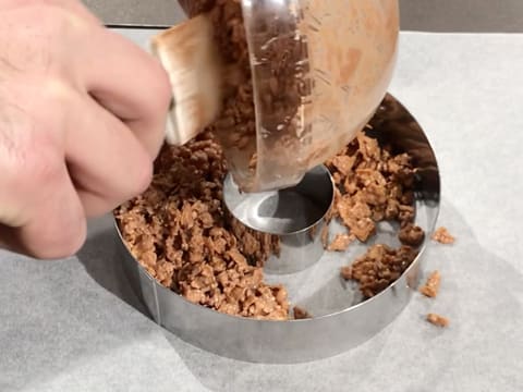 La pâte à palet croustillant est versée entre un grand cercle à mousse et un petit cercle à mousse qui a été placé au centre du premier, et sur une feuille de papier sulfurisé