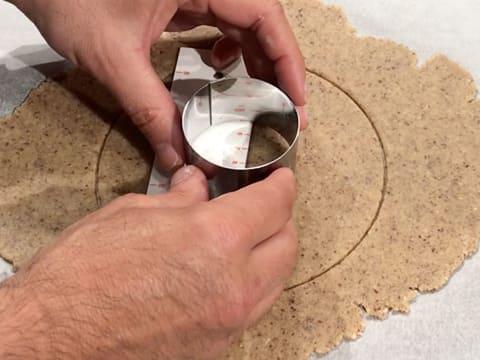 Le petit cercle à mousse est positionné au centre du grand disque de pâte à streusel noisette, avec l'utilisation d'une règle graduée