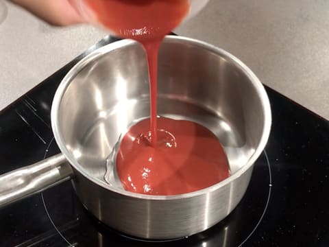 La purée de fraise est versée dans la casserole qui contient le sirop de glucose et le sucre inverti et qui est placée sur la plaque de cuisson