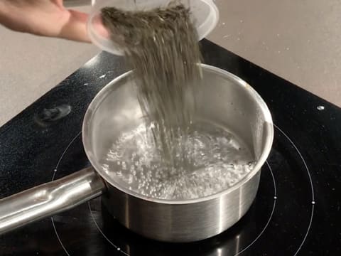 Les feuilles de thé au jasmin séchées sont versées dans la casserole contenant l'eau frémissante