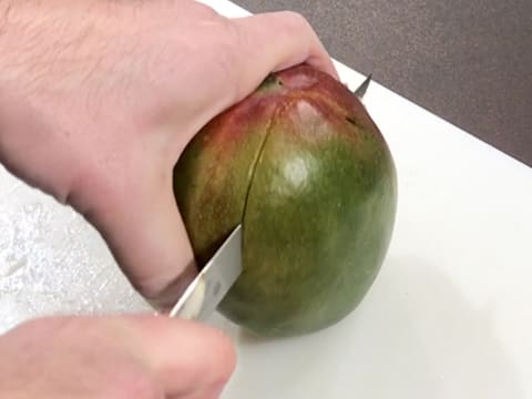 Sur une planche à découper, une mangue est coupée en deux dans la longueur à l'aide d'un couteau
