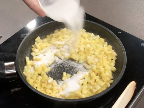 Du sucre en poudre est parsemé sur la brunoise de fruits dans la poêle qui est sur la plaque de cuisson