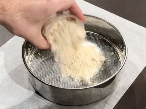 Le sucre en poudre et la poudre d'amandes sont tamisées dans un tamis, au-dessus d'une feuille de papier sulfurisé