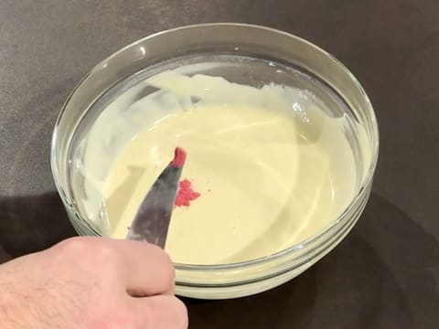 Ajout d'une pointe de couteau de colorant en poudre rose dans le chocolat blanc fondu dans le saladier sur le plan de travail