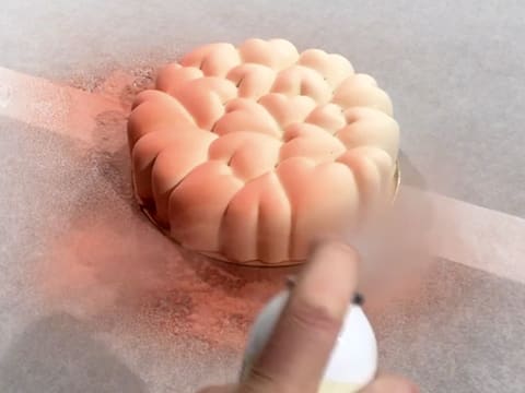 L'entremets placé sur des feuilles de papier sulfurisé, est pulvérisé de colorant en spray rose