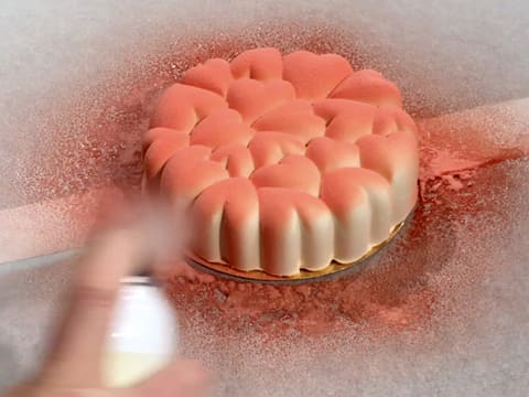 L'entremets placé sur des feuilles de papier sulfurisé, est pulvérisé de colorant en spray rose sur toute sa surface