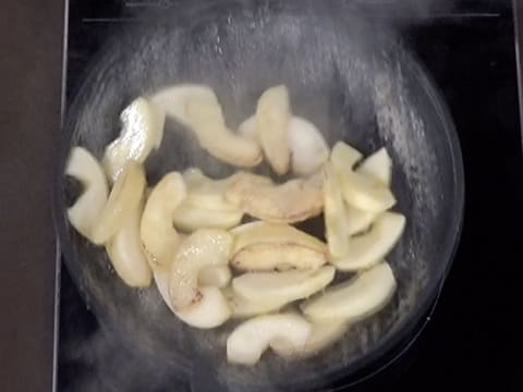 Les lamelles de pomme qui sont en train de cuire dans la poêle, sont remuées