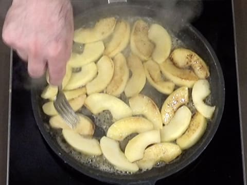 Les lamelles de pomme sont retournées dans la poêle, à l'aide d'une fourchette