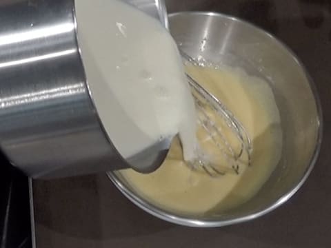 Un peu de mélange crème et lait chaud est versé dans le cul de poule sur la préparation oeufs, sucre et poudre à crème