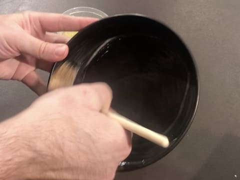 Un moule à manqué rond est graissé avec du beurre fondu à l'aide d'un pinceau à pâtisserie