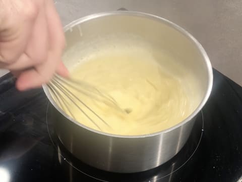 La crème pâtissière est en train de cuire dans la casserole, tout en étant mélangée au fouet