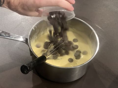 Les pistoles de chocolat noir sont versées dans la crème pâtissière chaude qui se trouve dans la casserole posée sur le plan de travail