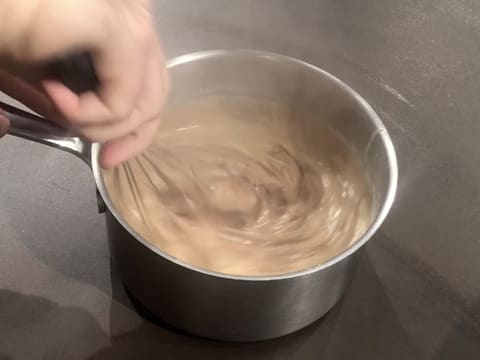 Mélange au fouet de la crème pâtissière chocolatée dans la casserole qui est posée sur le plan de travail