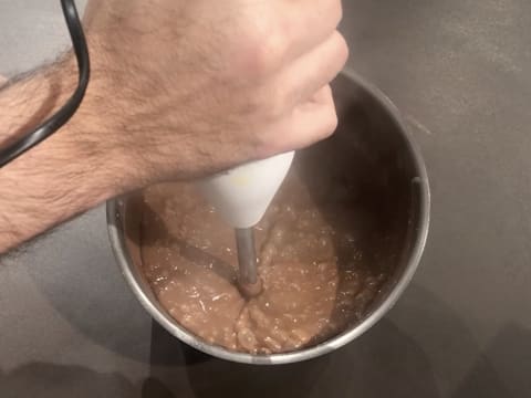 La crème pâtissière au chocolat est mixée à l'aide d'un mixeur plongeant dans la casserole qui est sur le plan de travail