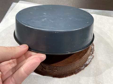 Le flan pâtissier au chocolat sans pâte est retourné sur le plan de travail recouvert d'une feuille de papier sulfurisé, et le moule à manqué rond est retiré vers le haut