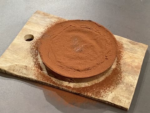 Obtention du flan pâtissier au chocolat sans pâte décoré du cacao en poudre, et qui est posé sur une planche à découper en bois