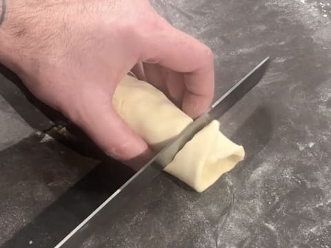 Une extrémité du boudin de pâte à brioche est coupée à l'aide d'un couteau scie à génoise