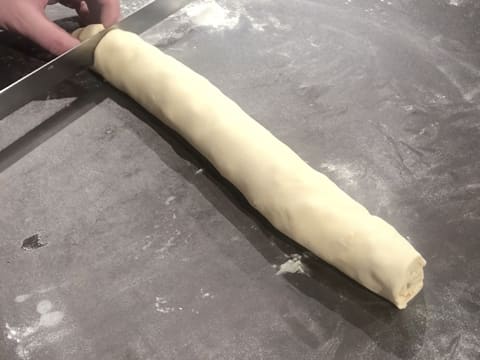 Une extrémité du boudin de pâte à brioche est coupée avec d'un couteau scie à génoise