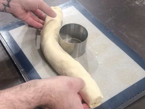 Le cercle à mousse graissé est posé sur une plaque à pâtisserie recouverte d'un tapis de cuisson en silicone, et le boudin de pâte à brioche commence à être enroulé autour du cercle inox