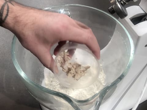 Ajout de la levure fraîche de boulanger sur la farine, le sel fin et le sucre en poudre dans la cuve du batteur
