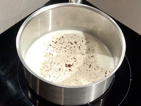 Une casserole contenant du lait et de la vanille en poudre est placée sur une plaque de cuisson