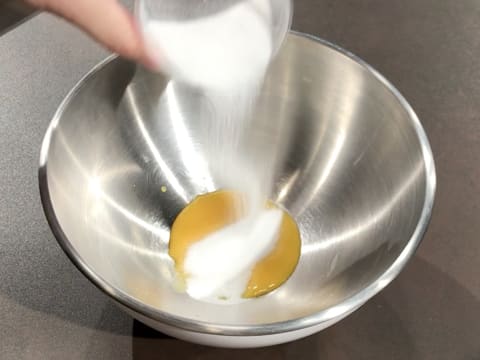 Du sucre en poudre est versé sur les jaunes d'oeufs dans un cul de poule