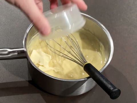 Ajout du beurre dans la crème qui est dans la casserole sur le plan de travail