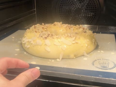 La pâte à brioche en forme de couronne et parsemée de crumble aux amandes et d'amandes effilées, est placée dans un four