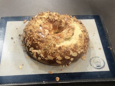 Obtention de la galette des rois briochée cuite et dorée, sur une plaque à pâtisserie recouverte d'un tapis de cuisson en silicone qui est posée sur le plan de travail