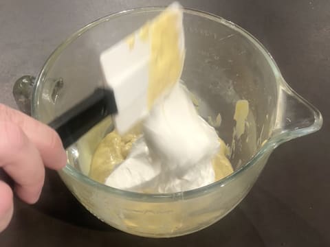 De la crème fouettée est versée dans la cuve du batteur qui est posée sur le plan de travail et qui contient la crème pâtissière