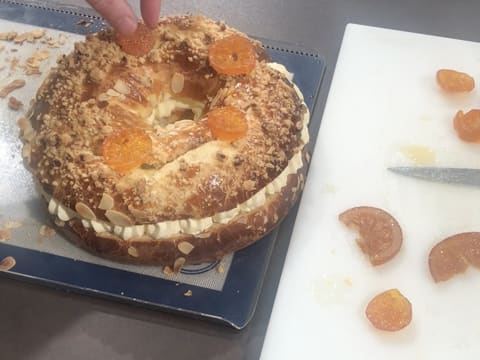 Des tranches de clémentines confites sont déposées sur la galette des rois briochée en forme de couronne, qui est fourrée à la crème diplomate