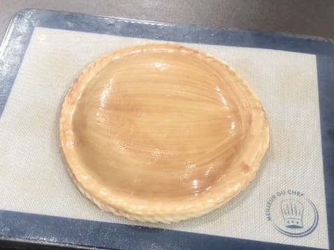 Obtention de la galette des rois entièrement badigeonnée de dorure au cacao et qui est posée sur une plaque à pâtisserie recouverte d'un tapis de cuisson en silicone