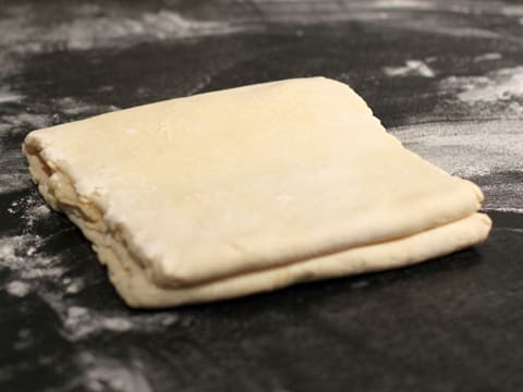 Le rectangle de pâte pliée en portefeuille est posé les plis sur les côtés, sur plan de travail fleuré