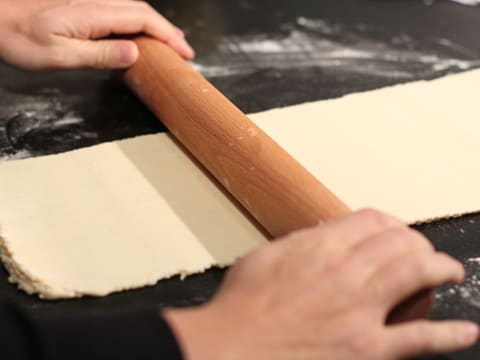 La pâte est abaissée en une longue bande avec le rouleau à pâtisserie sur le plan de travail fleuré