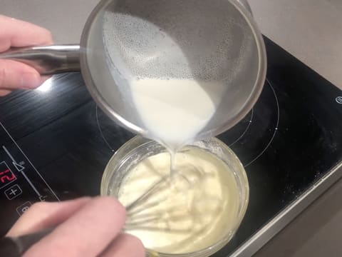 Du lait chaud est versé dans la préparation à base de jaunes d'oeufs, tout en étant mélangé au fouet