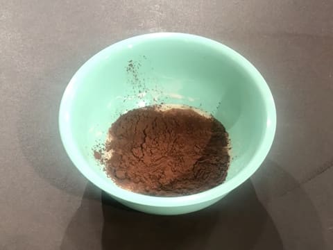 Ajout du cacao en poudre sur la crème fleurette qui est dans le bol posé sur le plan de travail