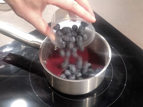 Les myrtilles sont versées dans la casserole qui contient la purée de cassis et qui est placée sur une plaque de cuisson